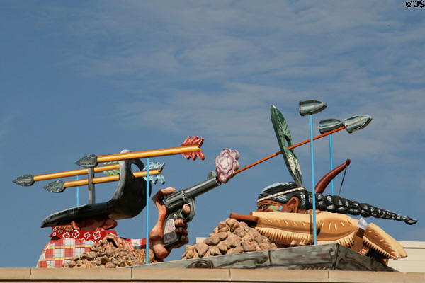 Comical sculpture of Cowboy & Indian firing gun & arrows at each other but missing on roof of section joining old & new wings of Denver Art Museum. Denver, CO.