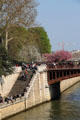 Pedestrians enjoying sunshine on quai of Seine River. Paris, France