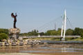 Pedestrian suspension bridge structure over Arkansas Rivers beyond Keeper of the Plains sculpture. Wichita, KS.
